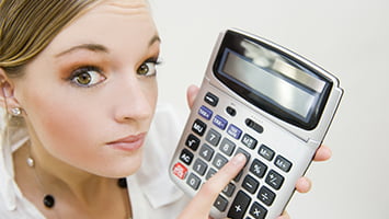 Une femme blonde tient à la main gauche une calculatrice.