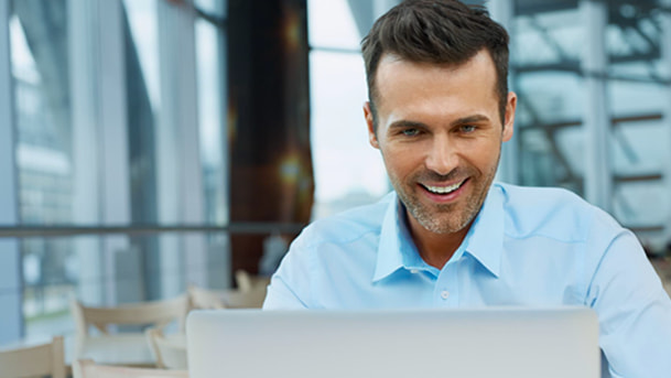 Un homme souriant habillé d'une chemise regarde l'écran de son ordinateur portable